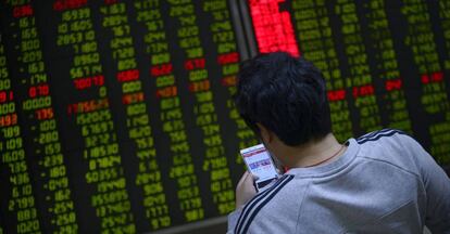 Un inversor mira su telefóno móvil frente a un panel de cotizaciones en Pekin. / AFP PHOTO / WANG Zhao