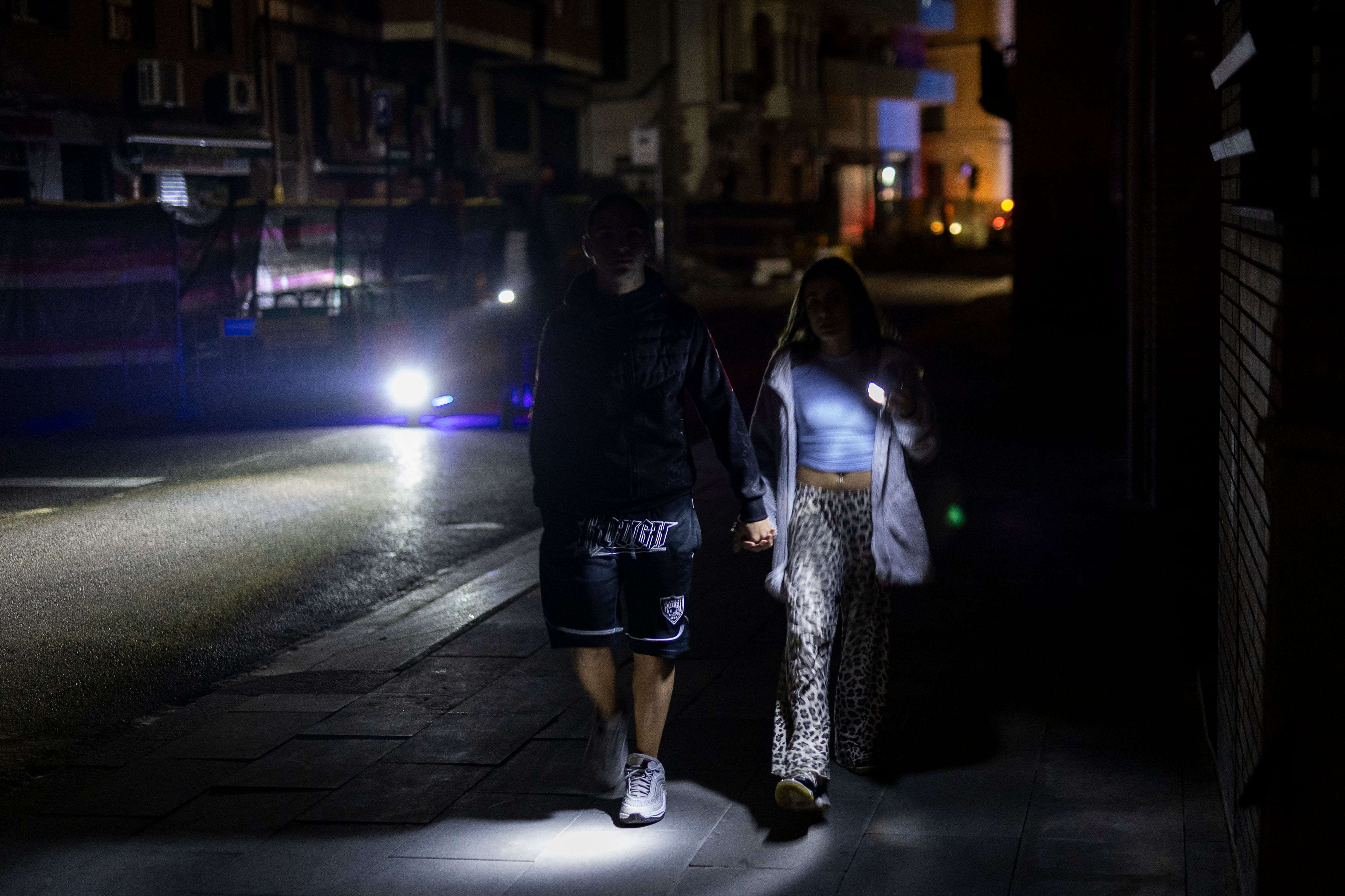 Una pareja camina a oscuras con la ayuda de la luz de una linterna por la calle Constitució absolutamente a oscuras el día del apagón, en Barcelona.
