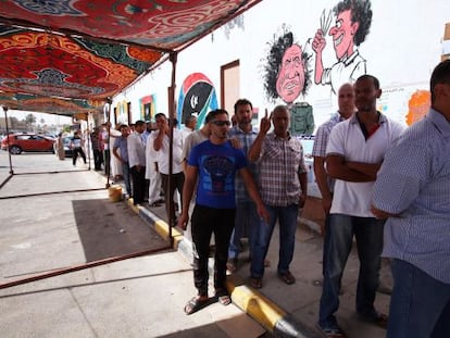Electores libios hacen cola junto a una caricatura de Mubarak en Tr&iacute;poli.