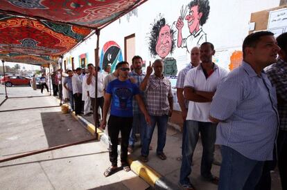 Electores libios hacen cola junto a una caricatura de Mubarak en Trípoli.