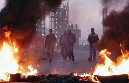 Un grupo de trabajadores, a la entrada al complejo petroquímico, cortada por una barricada incendiada.