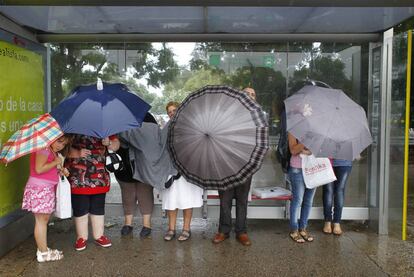 Varias personas se refugian del viento y el agua con sus paraguas bajo la marquesina de una parada de autobús.