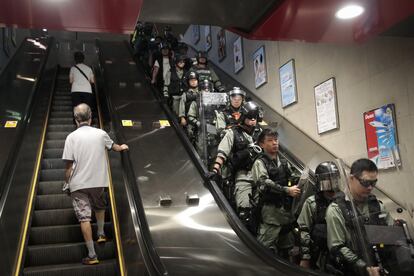 Dos viajeros suben por una escalera mecánica del metro frente a los oficiales antidisturbios desplegados para arrestar a los manifestantes en Hong Kong, el 2 de septiembre de 2019.