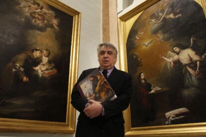 Enrique Valdivieso sostiene su libro junto a dos cuadros de Murillo, en el Bellas Artes de Sevilla.