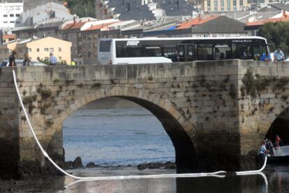 Varios agentes colocan barreras para frenar la mancha de combustible a la altura del puente romano de O Burgo.