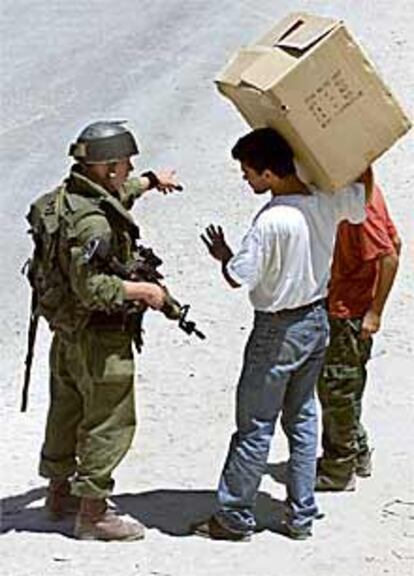 Un soldado ordena a dos palestinos pasar por un control en Qalandia.