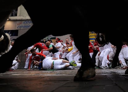 Corredores caen al suelo al pasa de los toros de la ganadería de Puerto de San Lorenzo durante el primer encierro de San Fermín.