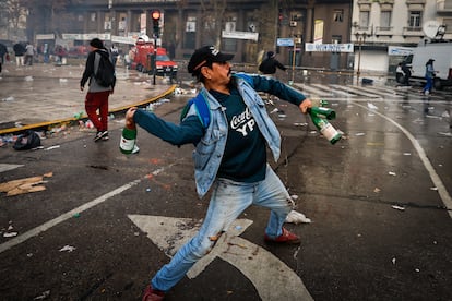 Un hombre se prepara para lanzar botellas de vidrio a los policías antidisturbios.