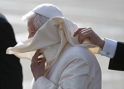 Un asistente personal del Papa Benedicto XVI, sujeta su capa movida por el fuerte viento, a su llegada al aeropuerto de Edimburgo en Escocia.