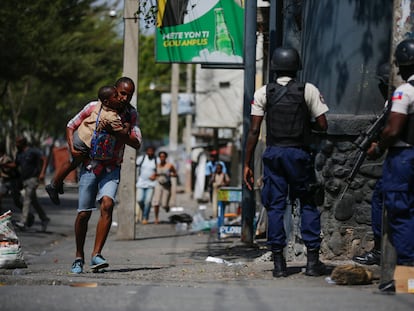 A parent carrying his child after picking him up from school, runs past police carrying out an operation against gangs in the Bel-Air area of Port-au-Prince, Haiti, on March 3, 2023.