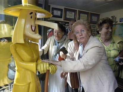 Una mujer toca las manos del muñeco que da nombre a la administración de lotería de Sort, La Bruixa d'Or (Lleida).