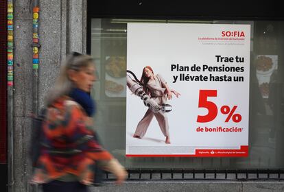 Una mujer pasa delante de un anuncio de planes de pensiones, en una oficina de Banco Santander, en Madrid.