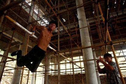 Un trabajador realiza una rutina en barra fija en un andamio mientras otros trabajadores graban con sus teléfonos móviles, en la zona de construcción de un templo budista, cerca de Quanzhou (China).