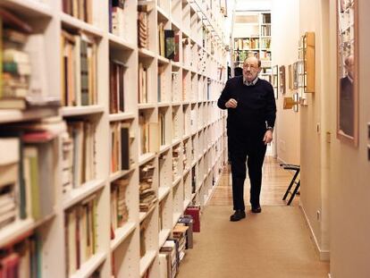 Umberto Eco caminha diante da estante de livros em sua casa.