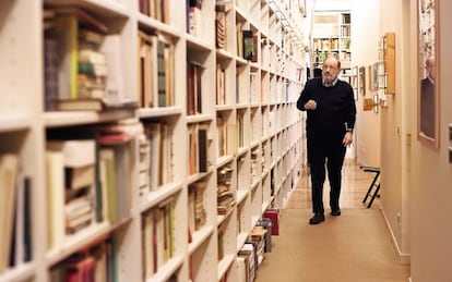 Umberto Eco caminha diante da estante de livros em sua casa.