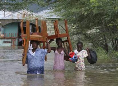 Tres habitantes de L'Artibonite, en el norte de Haití, transportan muebles sumergidos en las aguas vertidas por la tormenta tropical Hanna.