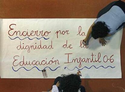 Dos profesores elaboran una de las pancartas de protesta que se colocarán en la escuela infantil El Rincón, de Leganés.