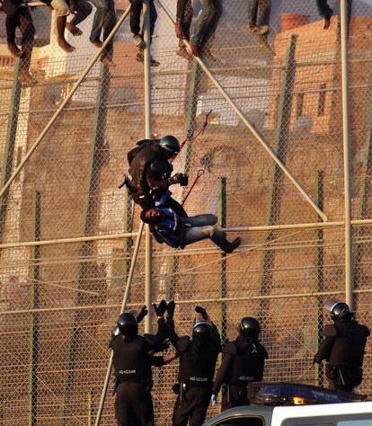 Un guardia civil baja de una verja a uno de los inmigrantes.