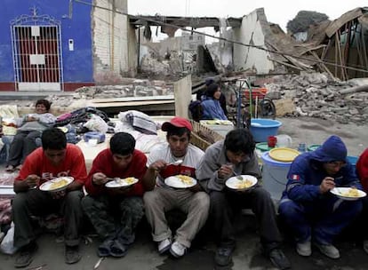 Víctimas del terremoto comen gracias a la ayuda humanitaria delante de los escombros de su casa en la ciudad de Pisco.