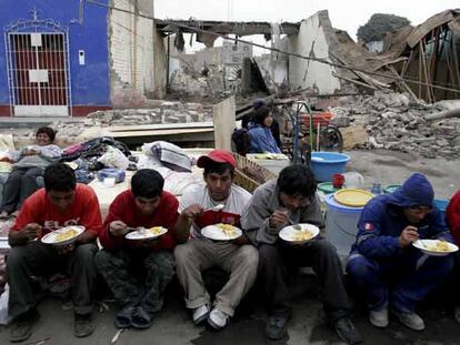 Víctimas del terremoto comen gracias a la ayuda humanitaria delante de los escombros de su casa en la ciudad de Pisco.