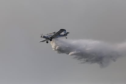 Una avioneta descarga agua para tratar de apagar un punto caliente del incendio forestal.