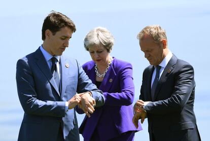 De izquierda a derecha, el primer ministro de Canadá, Justin Trudeau; la primera ministra del Reino Unido, Theresa May, y el presidente del Consejo Europeo Donald Tusk miran sus relojes antes de la foto de familia, el 8 de junio de 2018.