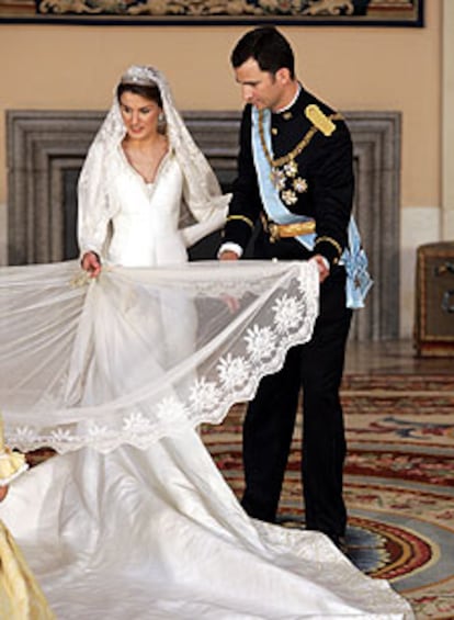 El príncipe Felipe ayuda a la princesa Letizia a colocar su vestido durante una sesión fotográfica.