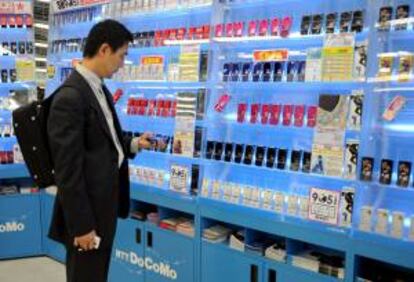 Un hombre revisa un dispositivo electrónico en una tienda junto a una estanteria llena de teléfonos móviles NTT DoCoMo en Tokio (Japón). EFE/Archivo