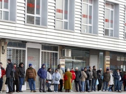 Varias personas forman una larga cola ante una oficina de empleo.