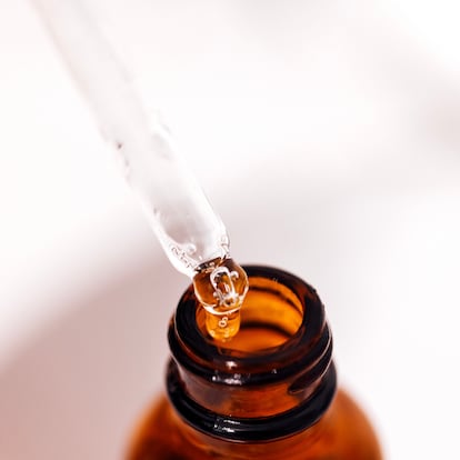 Close up of brown serum or oil glass with mock up on bottle on mirror background. Drops of liquid in a pipette. Concept of natural organic cosmetic and beauty, cosmetology, dermatology.