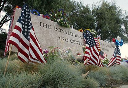 Flores y banderas,  ante el letrero de entrada a la biblioteca Ronald Reagan en Simi Valley (California).