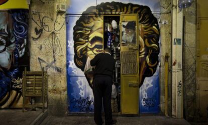 Un comerciante cierra las puertas de su establecimiento en el mercado Mahane Yehuda, decorado con un grafiti del artista callejero Solomon Souza, en Jerusalén.
