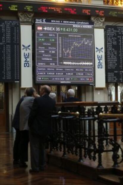 Un grupo de inversores observa en el parqu&eacute; madrile&ntilde;o el panel informativo que muestra la evoluci&oacute;n del IBEX 35.