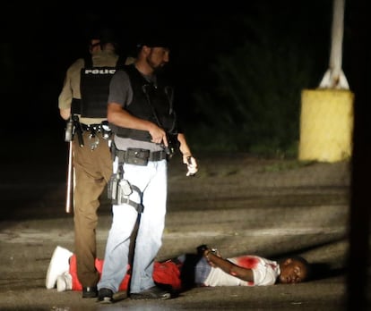 Dos policías junto a un herido tras el tiroteo que ha tenido lugar durante la marcha por el primer aniversario de la muerte del joven negro Michael Brown, en Ferguson, Misuri.