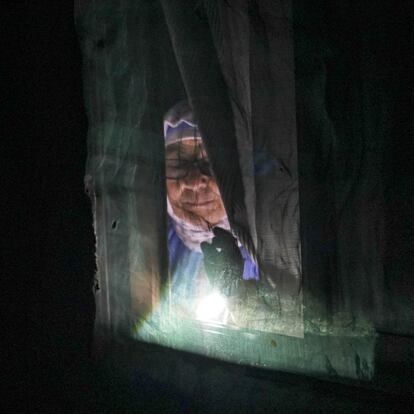 Una mujer se asoma por la ventana de su casa iluminada por la luz de una linterna en el sector seis de la Cañada Real Galiana, el mayor asentamiento irregular de Europa.