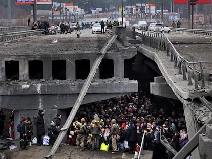 Ucranios intentan pasar por debajo de un puente destruido en Irpin, cerca de Kiev, este sábado.