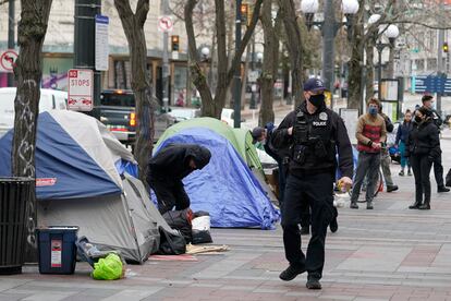 A Seattle police officer walks past tents used by people experiencing homelessness, March 11, 2022, during the clearing and removal an encampment in Westlake Park in downtown Seattle.