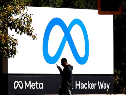 Un hombre consulta su móvil frente a un cartel de Meta en la sede de Facebook en California.