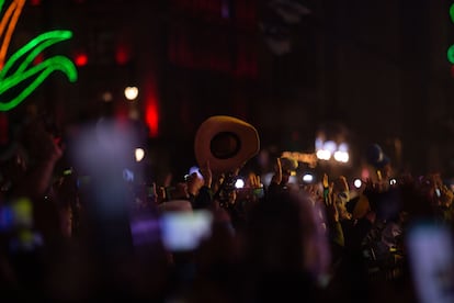 Una mano se asoma por encima de la multitud, agitando un sombrero.