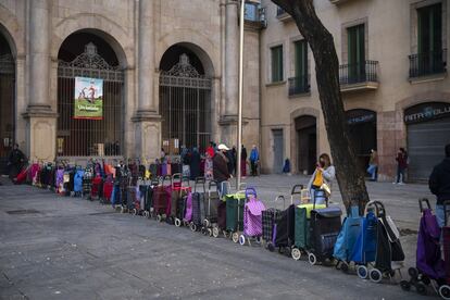 Carritos colocados en fila por sus dueños que esperan recibir un paquete semanal de alimentos y suministros donados, frente a una iglesia en Barcelona.