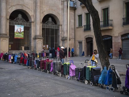 Carritos colocados en fila por sus dueños que esperan recibir un paquete semanal de alimentos y suministros donados, frente a una iglesia en Barcelona.