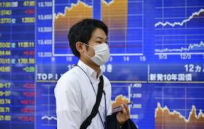 Un hombre camina junto a una pantalla con información bursátil en Tokio (Japón).