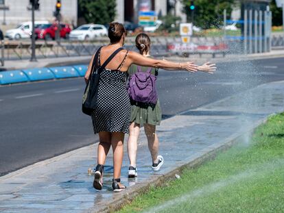 Dos mujeres se mojan con unos chorros de aspersores, a 21 de agosto de 2023, en Madrid.
