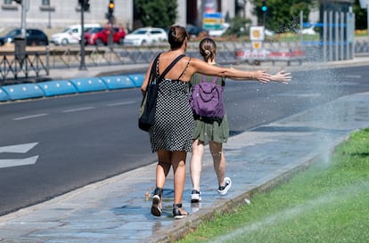 Dos mujeres se mojan con unos chorros de aspersores, a 21 de agosto de 2023, en Madrid.