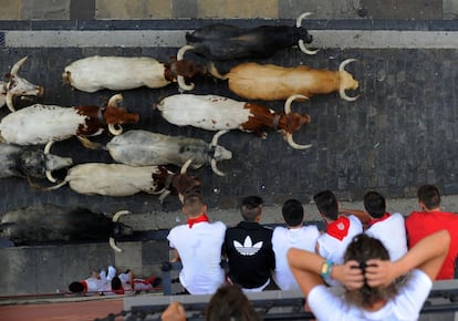 Varias personas miran el primer encierro de San Fermín desde los balcones de una de las calles.
