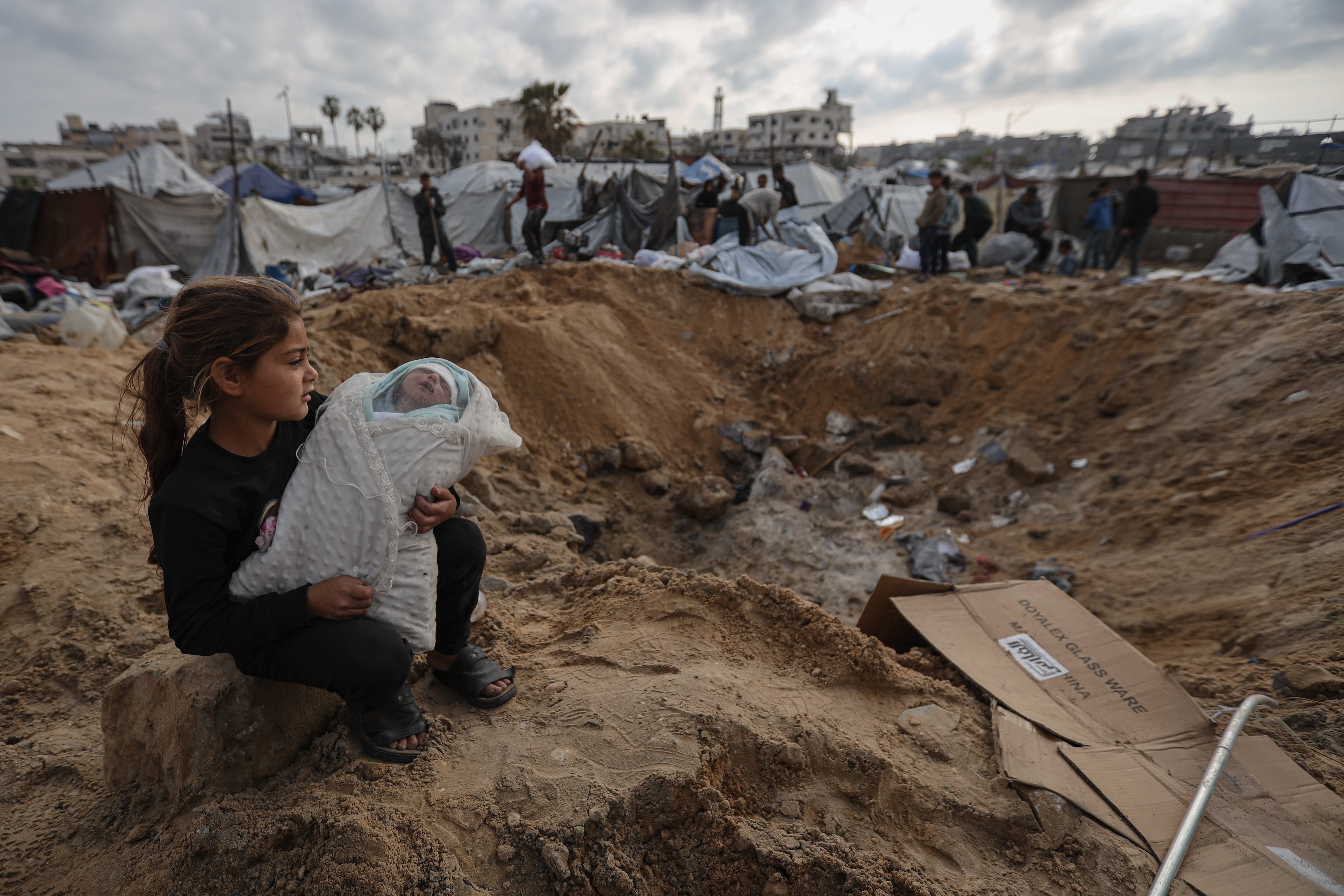 Una niña sostiene a un bebé mientras los palestinos buscan objetos personales entre los escombros tras el ataque israelí contra tiendas de campaña improvisadas en la zona de Ensar, en la ciudad de Gaza, este jueves.