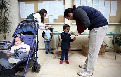 Los colegios han abierto a las 9.00 para los décimos comicios andaluces. En la imagen, unos padres con sus hijos cogen las papeletas antes de la votar.