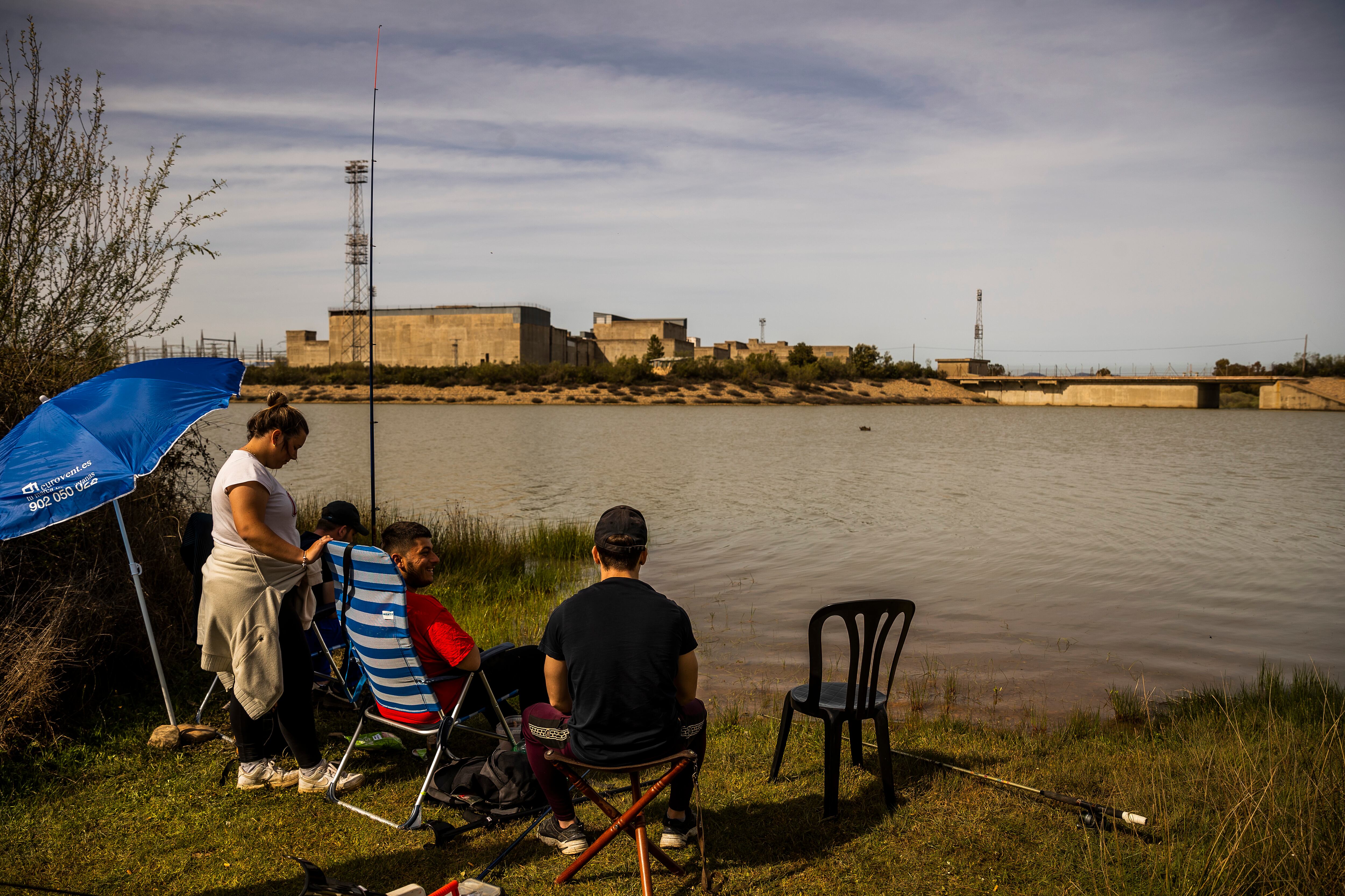 Varios jóvenes pescan con la central nuclear de Valdecaballeros de fondo. 