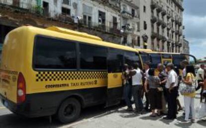 Varias personas hacen fila para subir a un ómnibus de una cooperativa de taxis colectivos  en La Habana (Cuba).