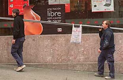 Dos trabajadores portan una bolsa ante un cartel de Euskal Herritarrok.